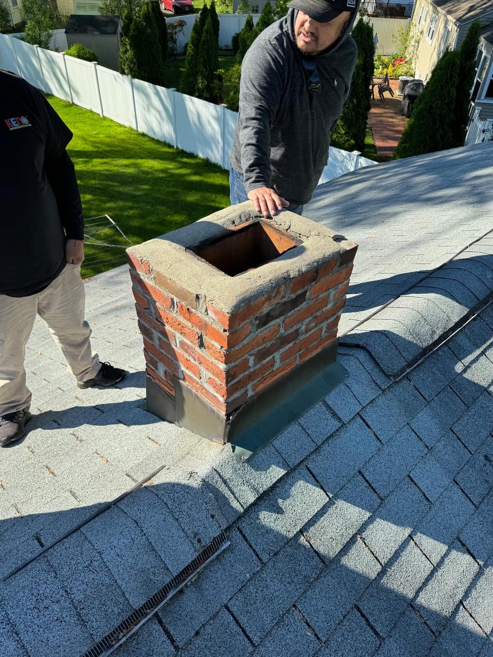 New step flashing installed around a brick chimney on a shingle roof